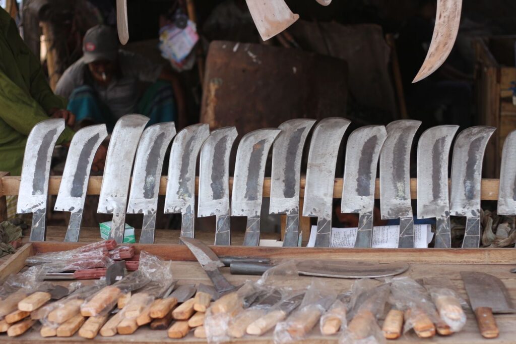 A collection of artisanal knives and tools displayed on a wooden table at an outdoor market.