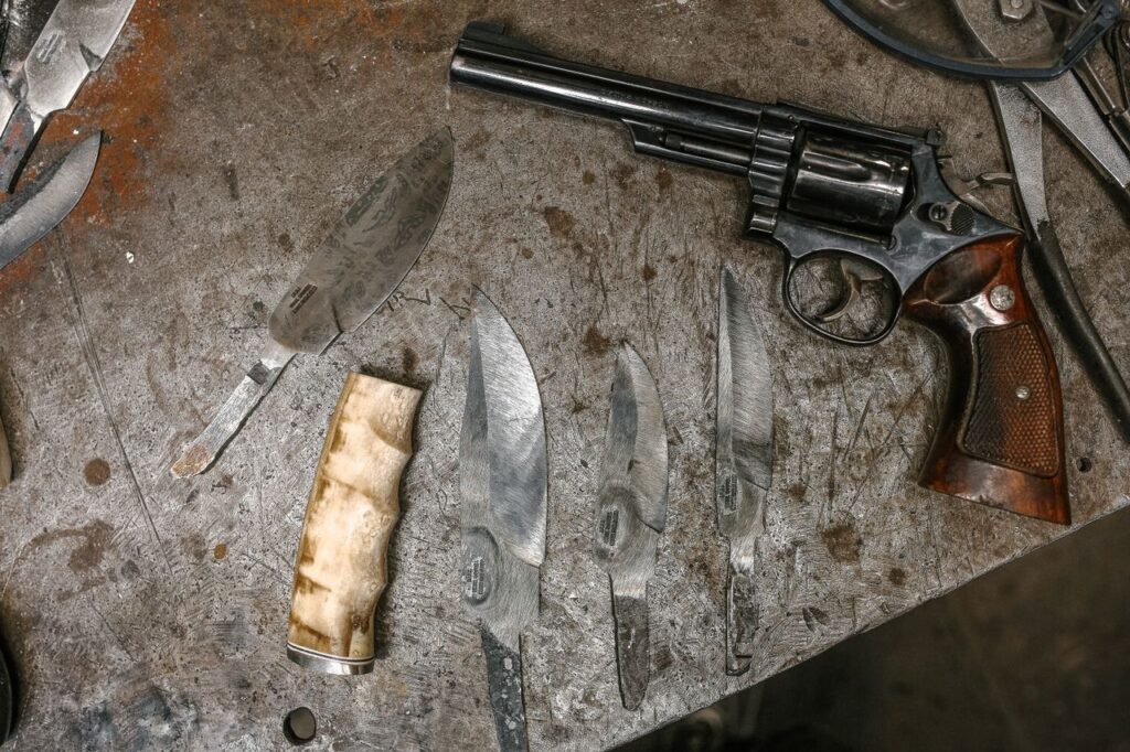 Variety of knives and a revolver placed on a workshop table in a flat lay setup.